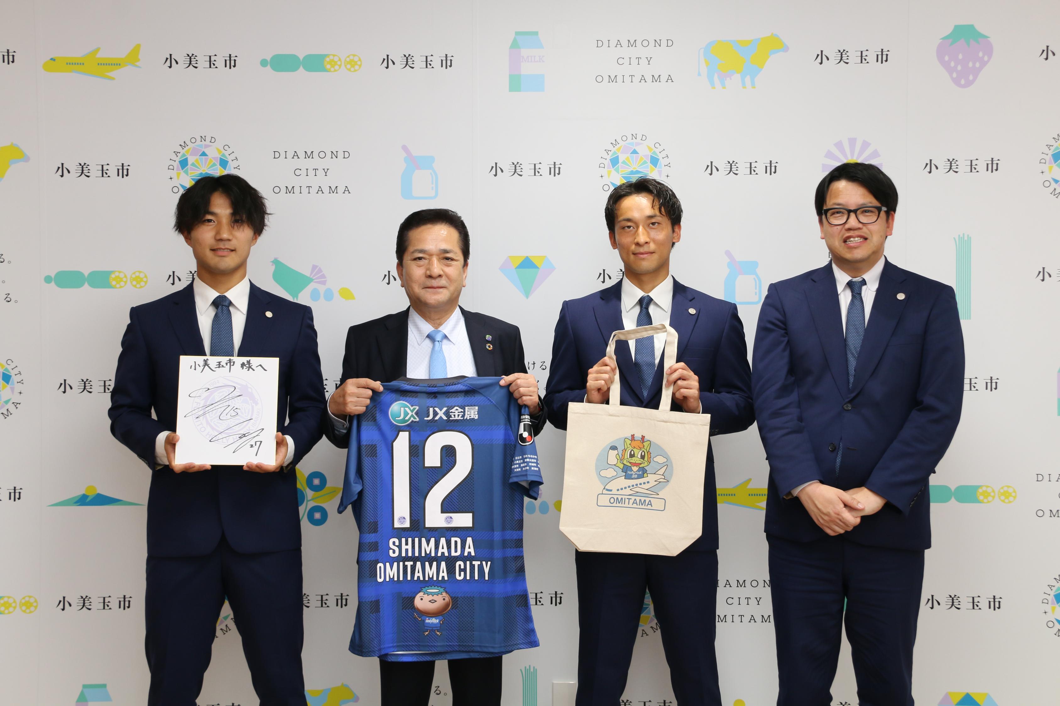 ユニフォームを持ち集合写真を撮る市長